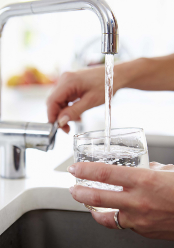 Manos de mujer cogiendo agua de un grifo de cocina en un vaso